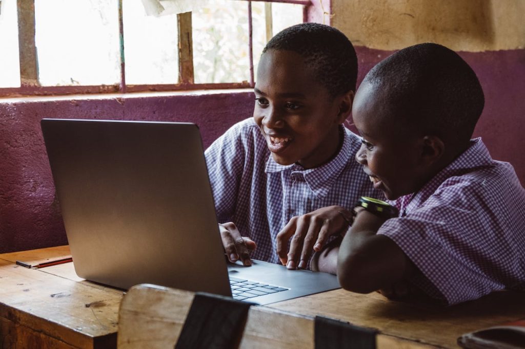 Smiling children learning together using a laptop indoors in a classroom setting.