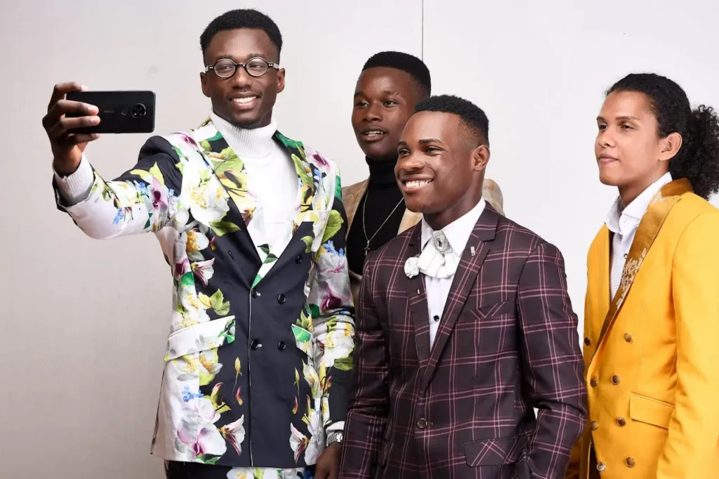 Group of fashionable young men in colorful suits taking a selfie indoors with smiles.